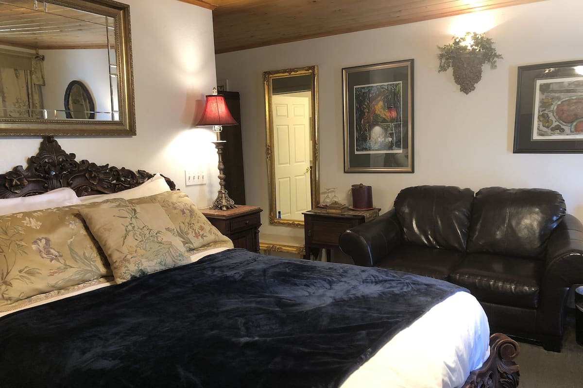 A bedroom with a large bed, a leather armchair, a wooden headboard, a nightstand with a lamp, and framed artwork on the walls.