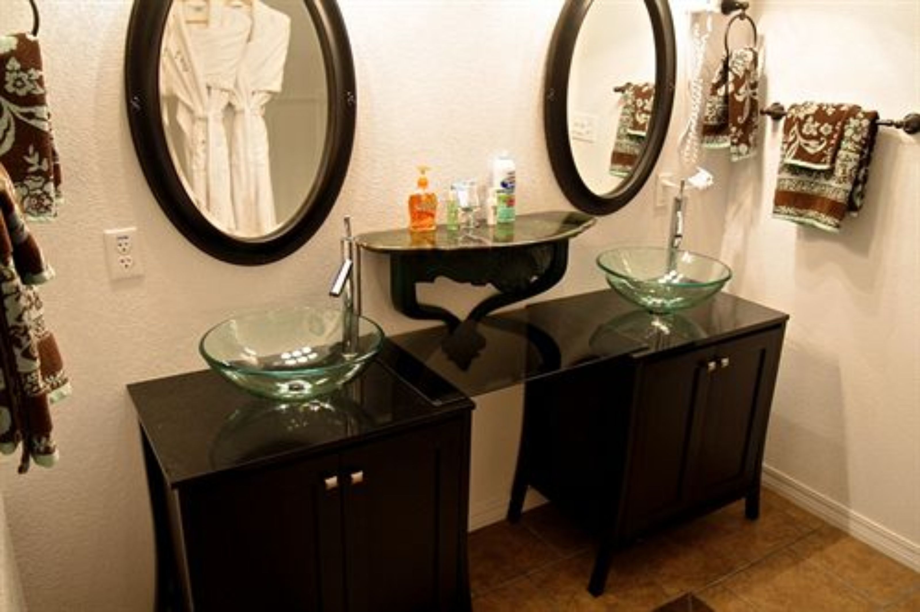 Une salle de bain avec deux meubles noirs, un lavabo en forme de bol en verre et deux miroirs ronds.