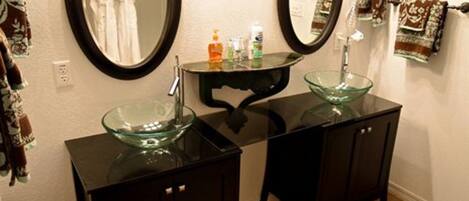 Une salle de bain avec deux meubles noirs, un lavabo en forme de bol en verre et deux miroirs ronds.