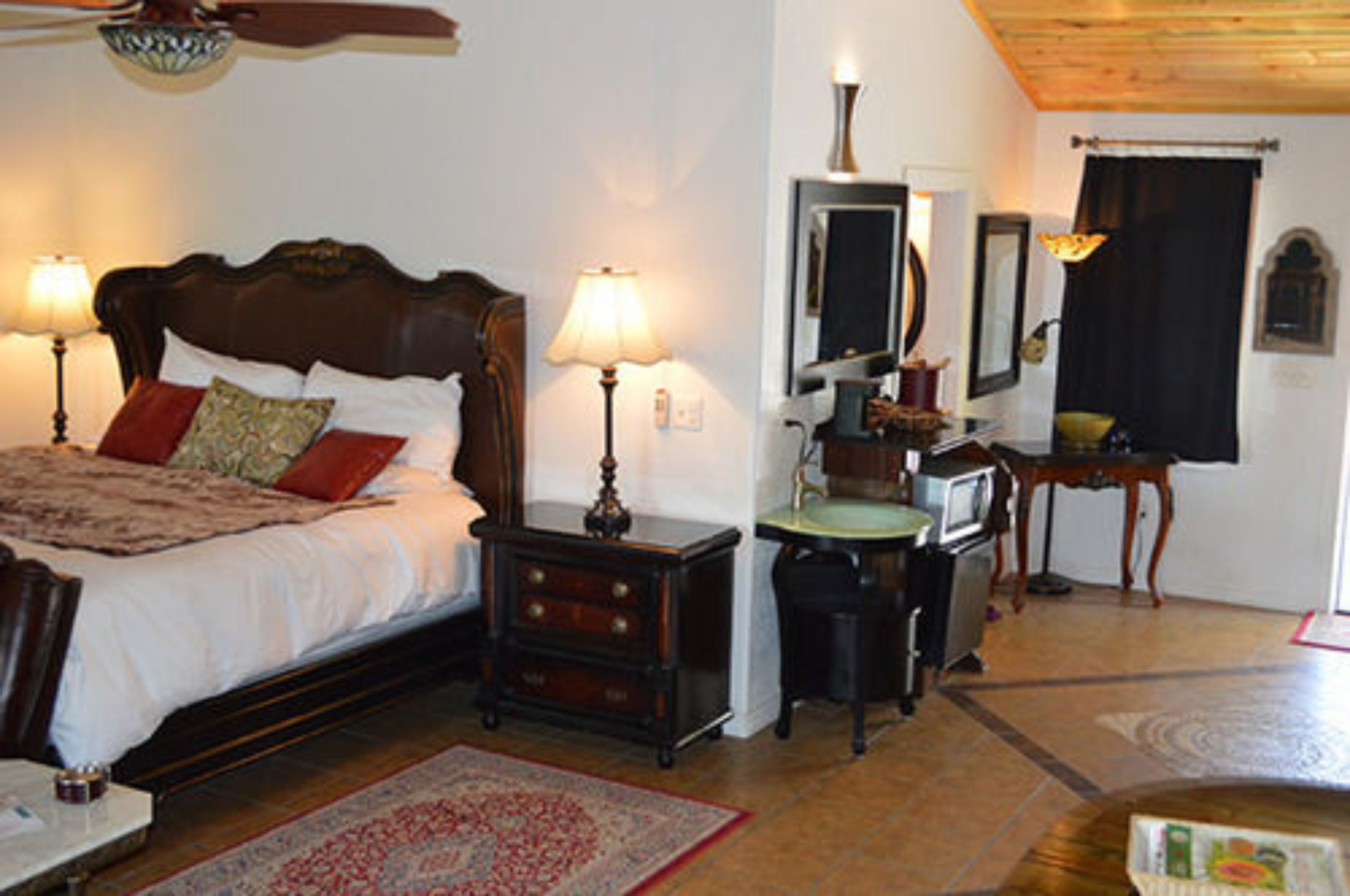A bedroom with a wooden bed, two bedside lamps, a nightstand, a dresser, a mirror, a television, and a small table with a lamp.