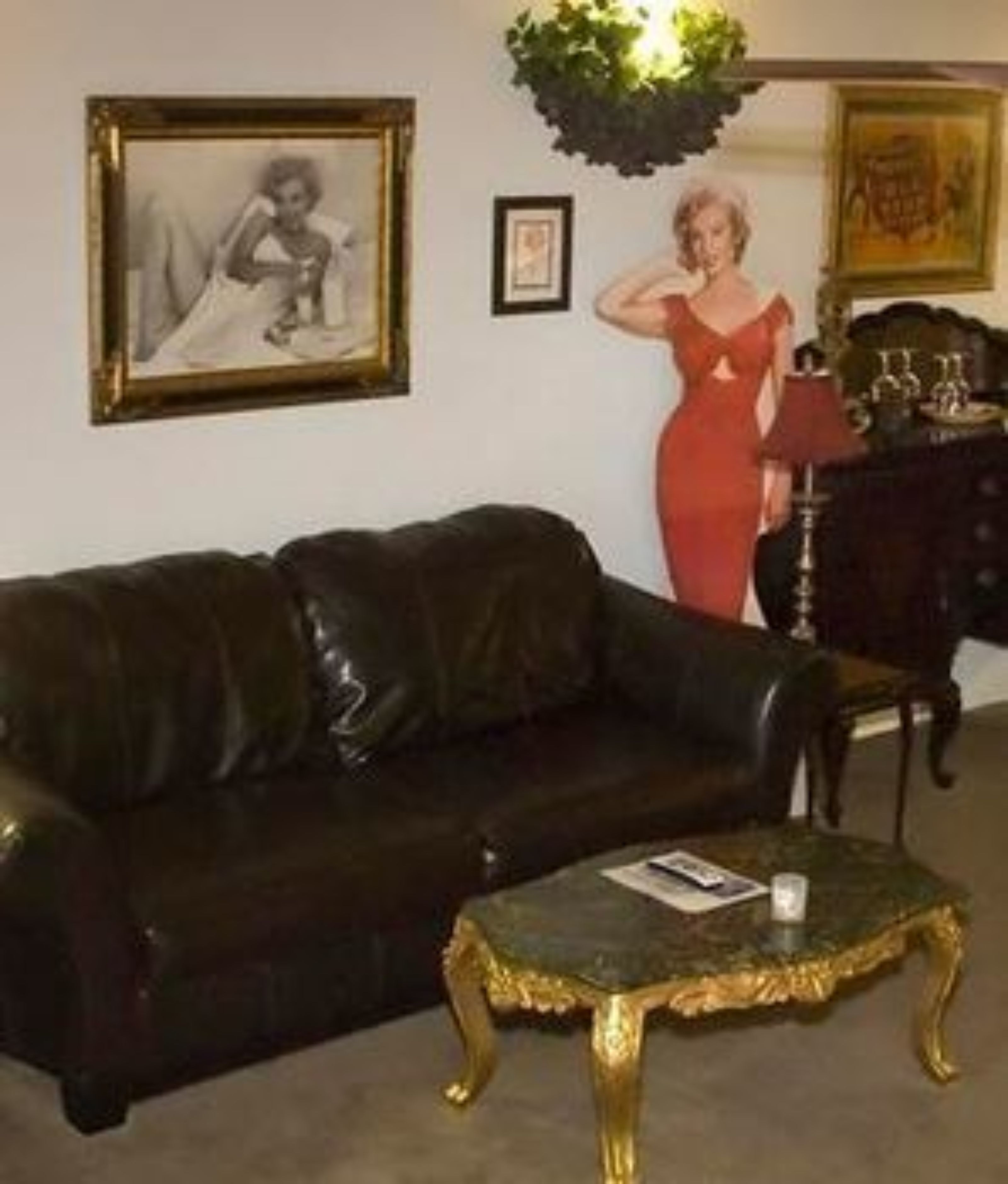 A living room with a dark leather couch, a small round table with a glass top, and a red dress hanging on the wall.