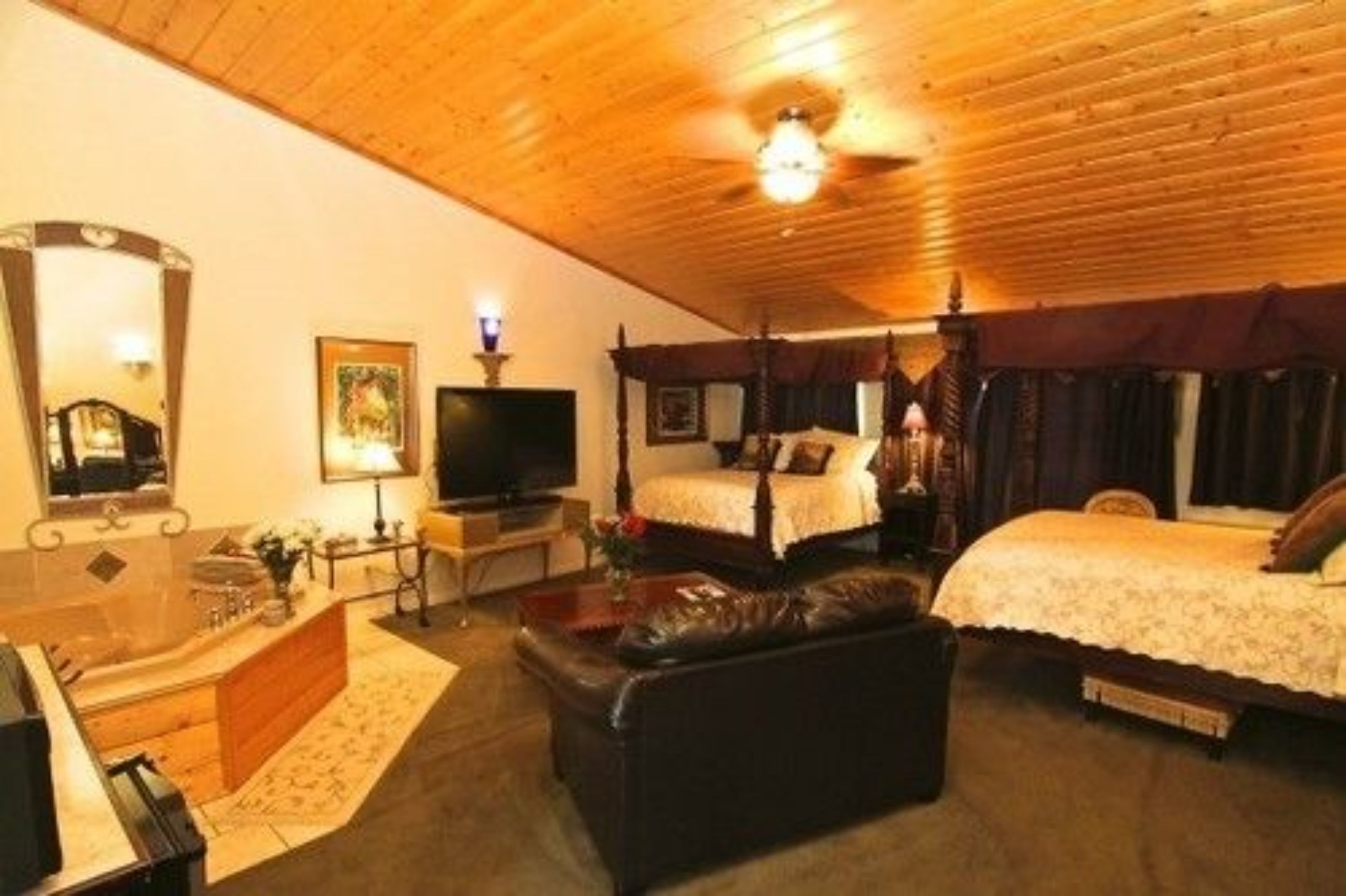 Une pièce avec un plafond en bois, un grand lit à baldaquin, une télévision, un bureau et un canapé en cuir.