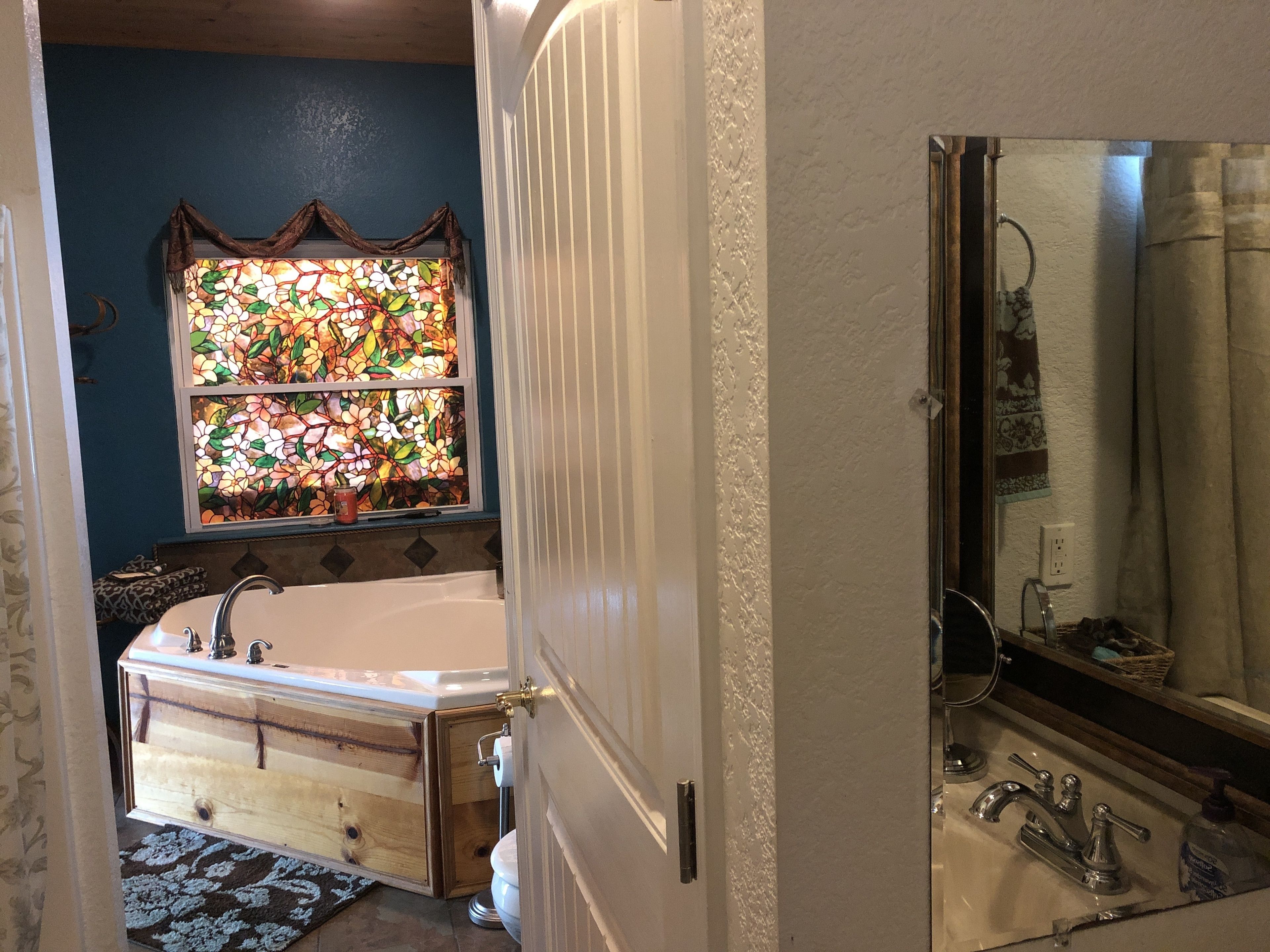 Un baño con bañera, espejo, lavabo y un vitral.
