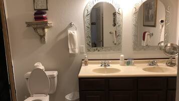 A bathroom with a toilet, two sinks, a vanity, and a large mirror with decorative frames.