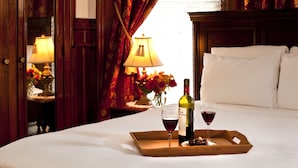 A hotel room with a bed, a bedside table with a lamp, a tray with a bottle of wine and a glass, and a vase with flowers. - American Guest House (Washington)