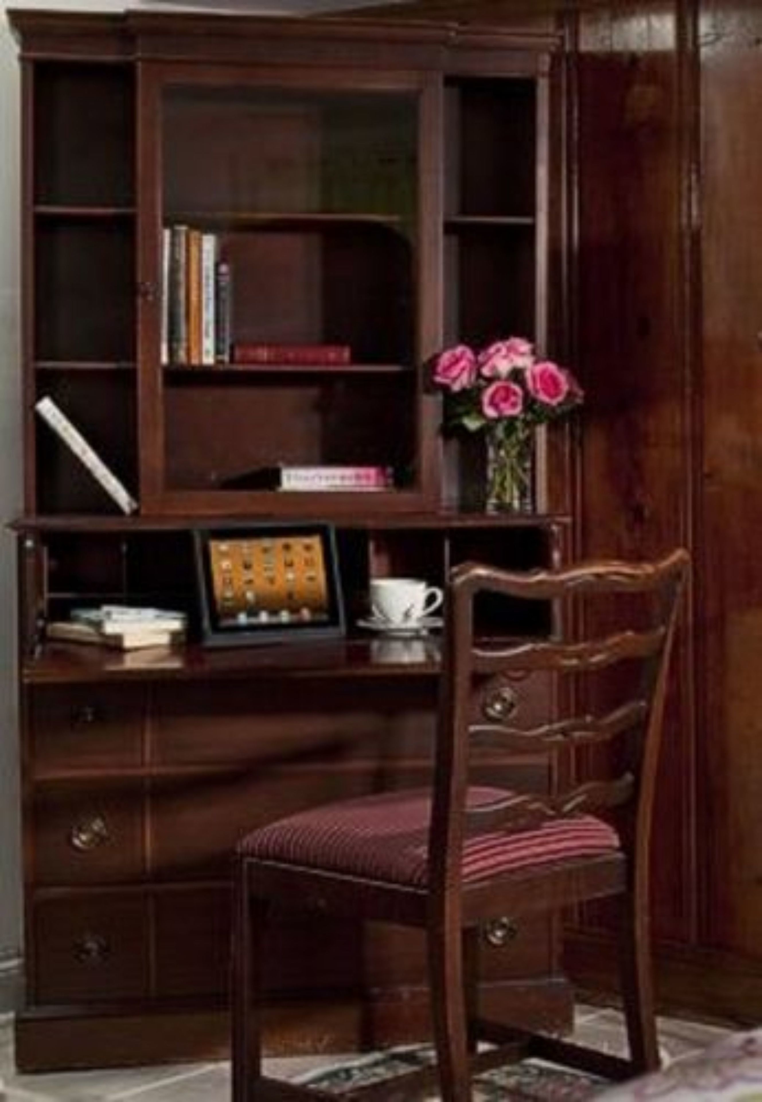 Een houten bureau met een stoel, een boekenkast en een vaas met bloemen.