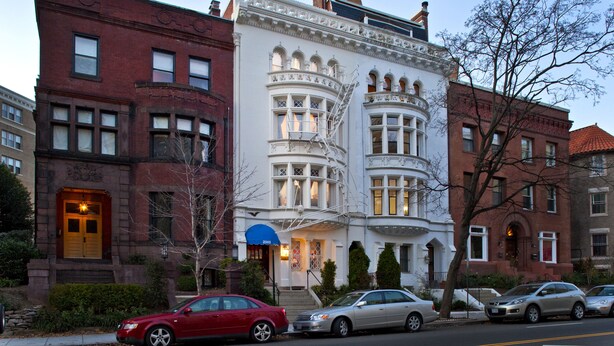 A historic building with a prominent corner entrance, a fire escape, and a well-lit facade. - American Guest House (Washington)
