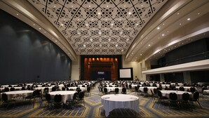 A large conference room with multiple round tables and chairs, a patterned ceiling, and a stage with a screen at the front. - American Guest House (Washington)