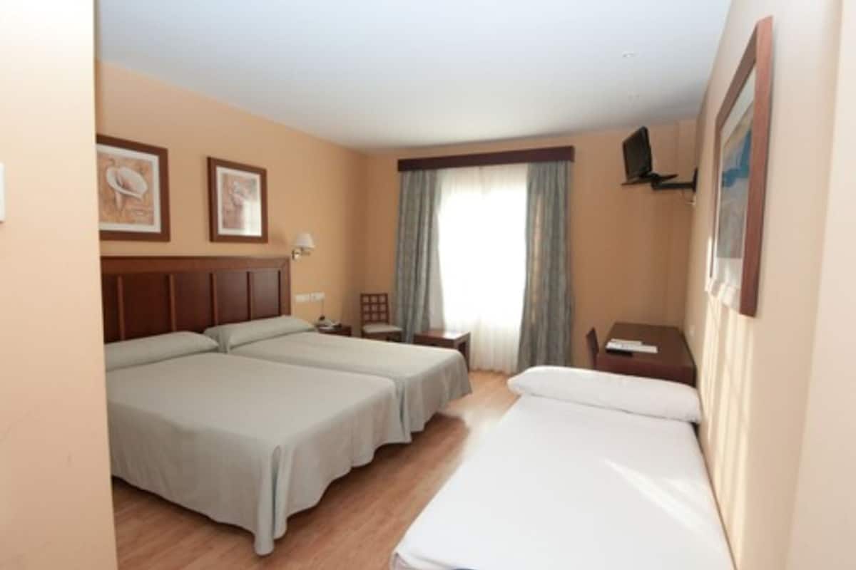 Habitación de hotel con dos camas, un escritorio, una silla, un televisor y una ventana con cortinas.