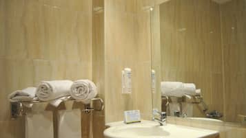 Un baño con pared de mármol, un lavamanos y un perchero con toallas dobladas.