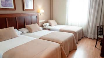 Habitación de hotel con dos camas, un cabecero de madera, una mesita de noche, una lámpara y una silla.