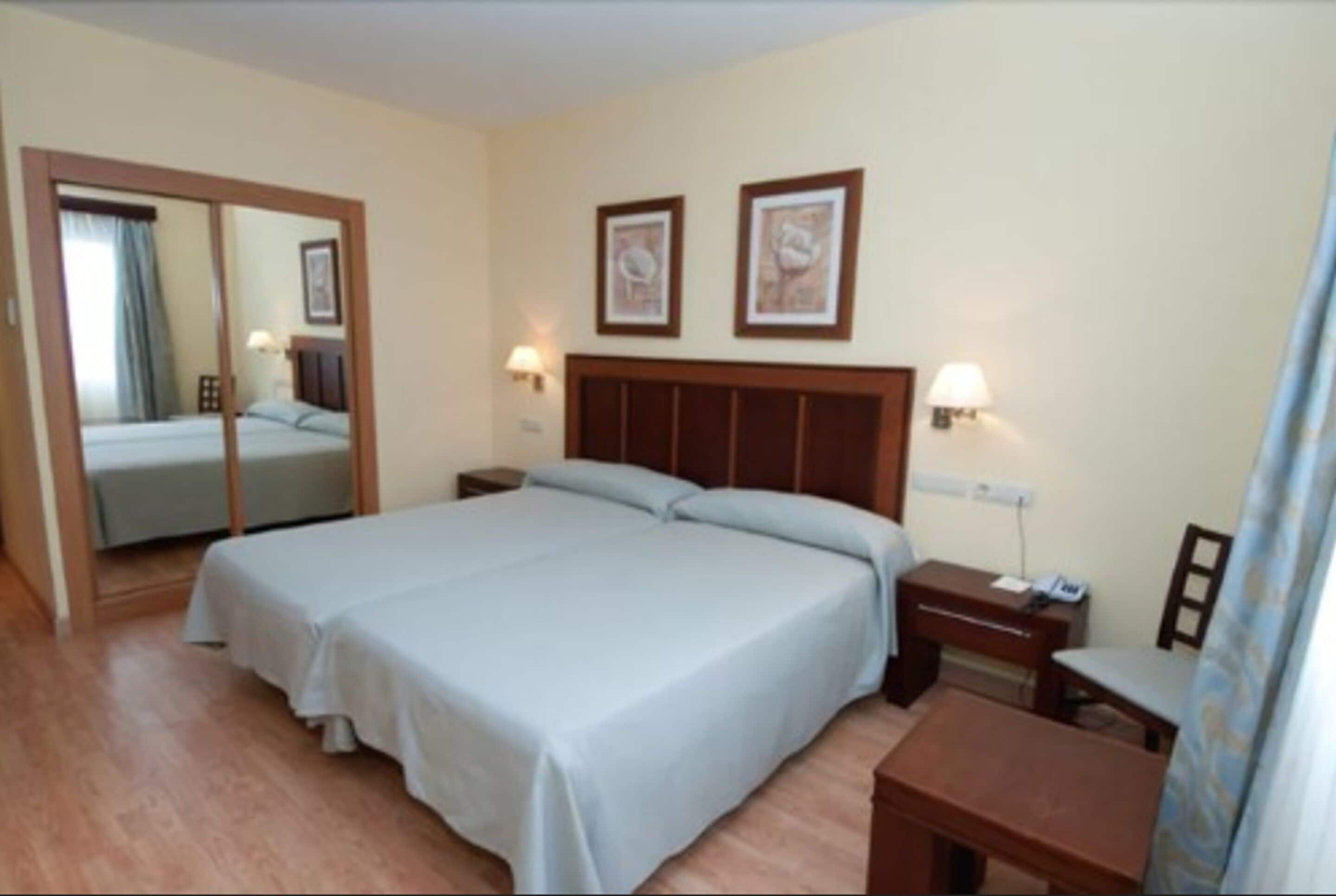 A hotel room with a large bed, a bedside table, a desk, and a mirror.