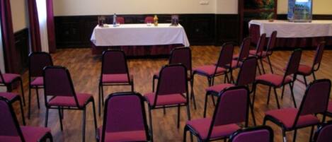 Un salón de conferencias con una mesa blanca, sillas moradas y suelo de madera.