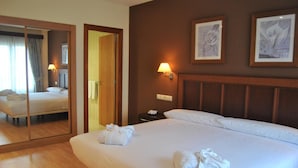 A hotel room with a large bed, a bedside table with a lamp, a mirror, and two framed artworks on the wall. - Hotel Santiago de León (Villaquilambre)