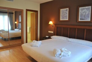 Una habitación de hotel con una cama grande, una mesita de noche con lámpara, un espejo y dos cuadros enmarcados en la pared.