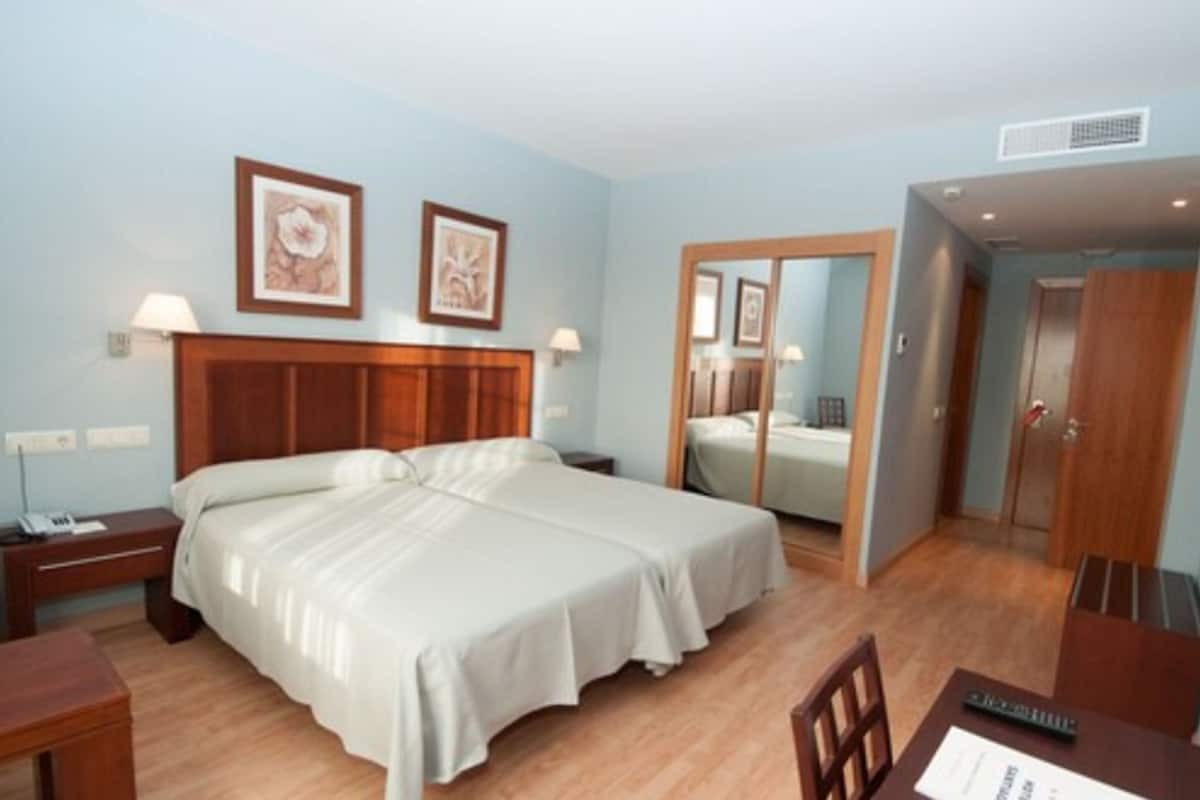 Una habitación de hotel con una cama grande, mesitas de noche, un escritorio y un espejo.