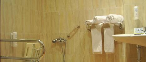 Un baño con ducha, barra de apoyo, toallero con toallas y lavabo con artículos de aseo.