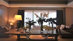 A modern hotel lobby with a seating area, a coffee table with vases, and a view of the street through large windows. - Hotel Santiago de León (Villaquilambre)