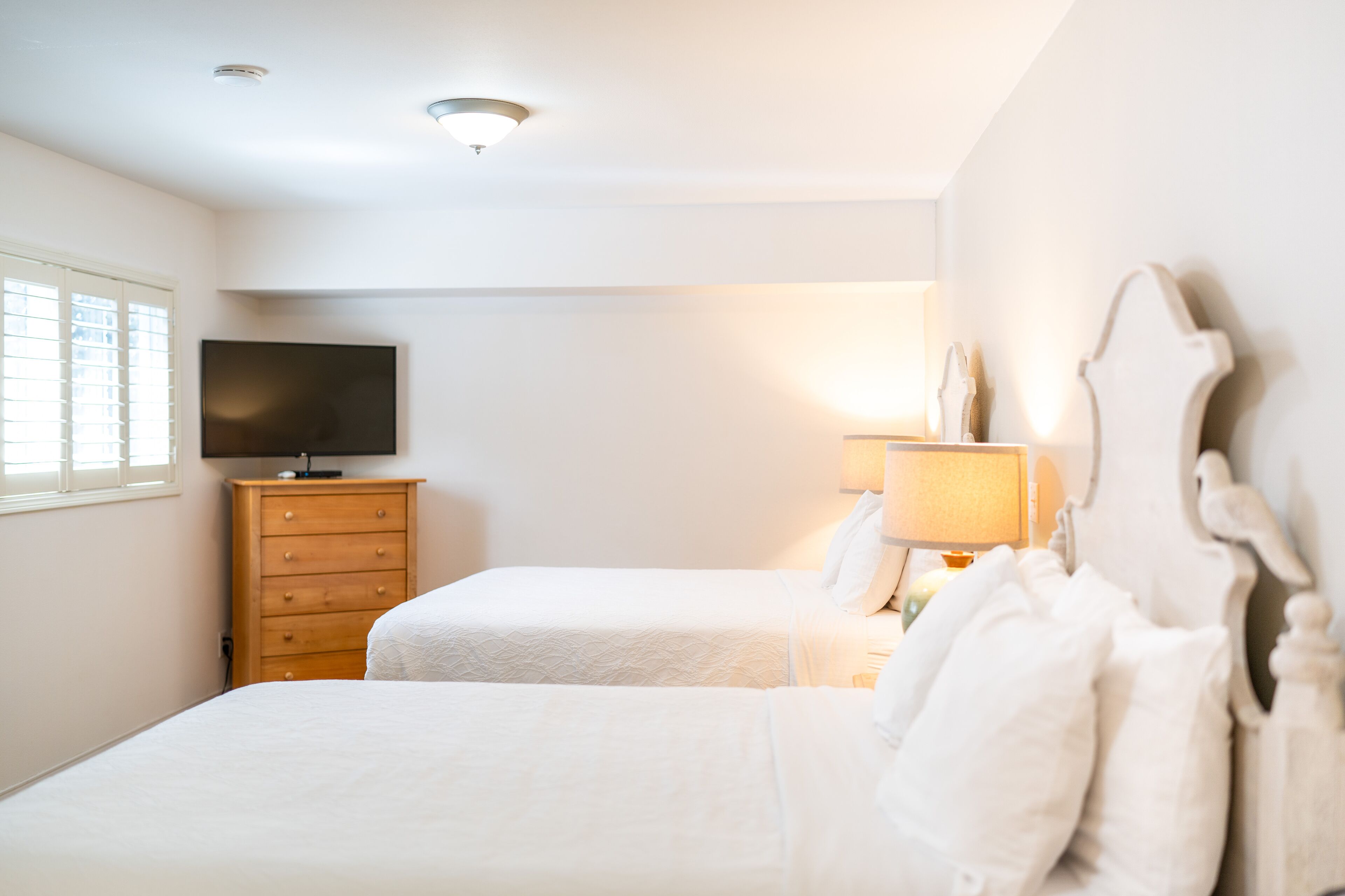 A bedroom with two beds, a wooden dresser, a television, and a lamp.