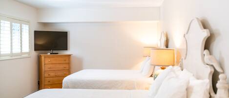 A bedroom with two beds, a wooden dresser, a television, and a lamp.