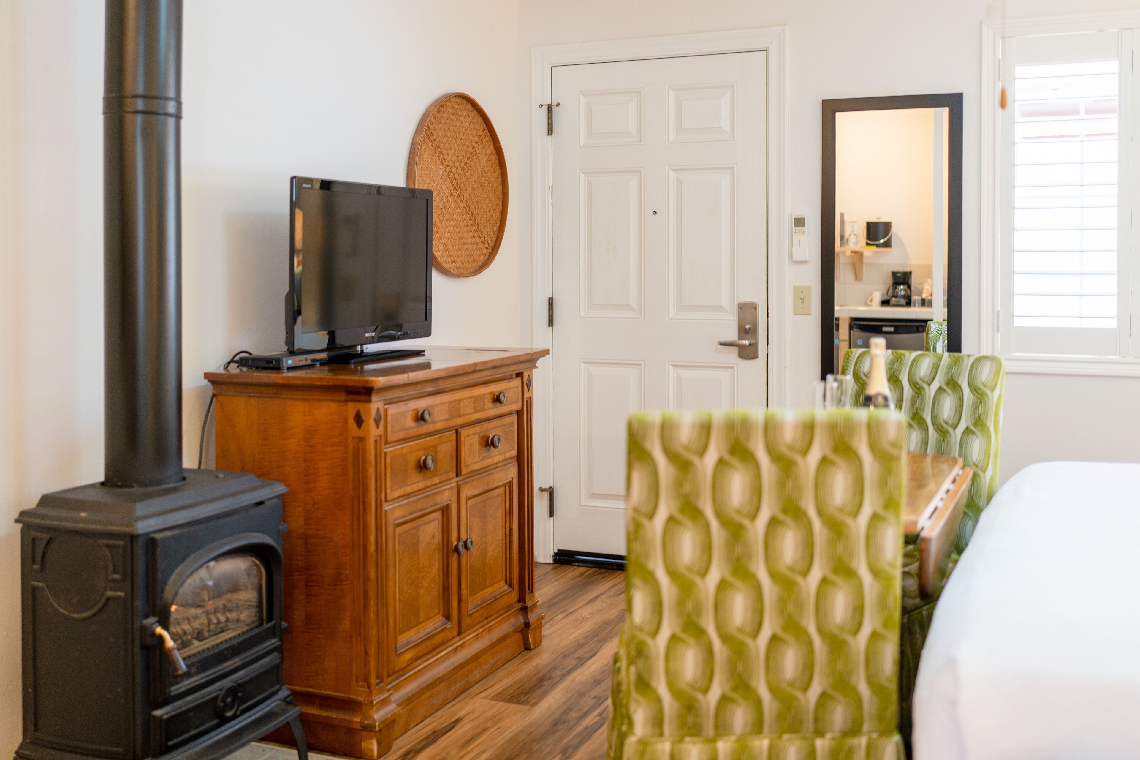 A room with a wood-burning stove, a television on a wooden cabinet, a green upholstered chair, and a white door.