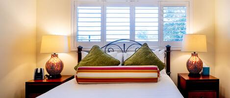 A neatly made bed with striped bedding, two green pillows, and two lamps on nightstands.