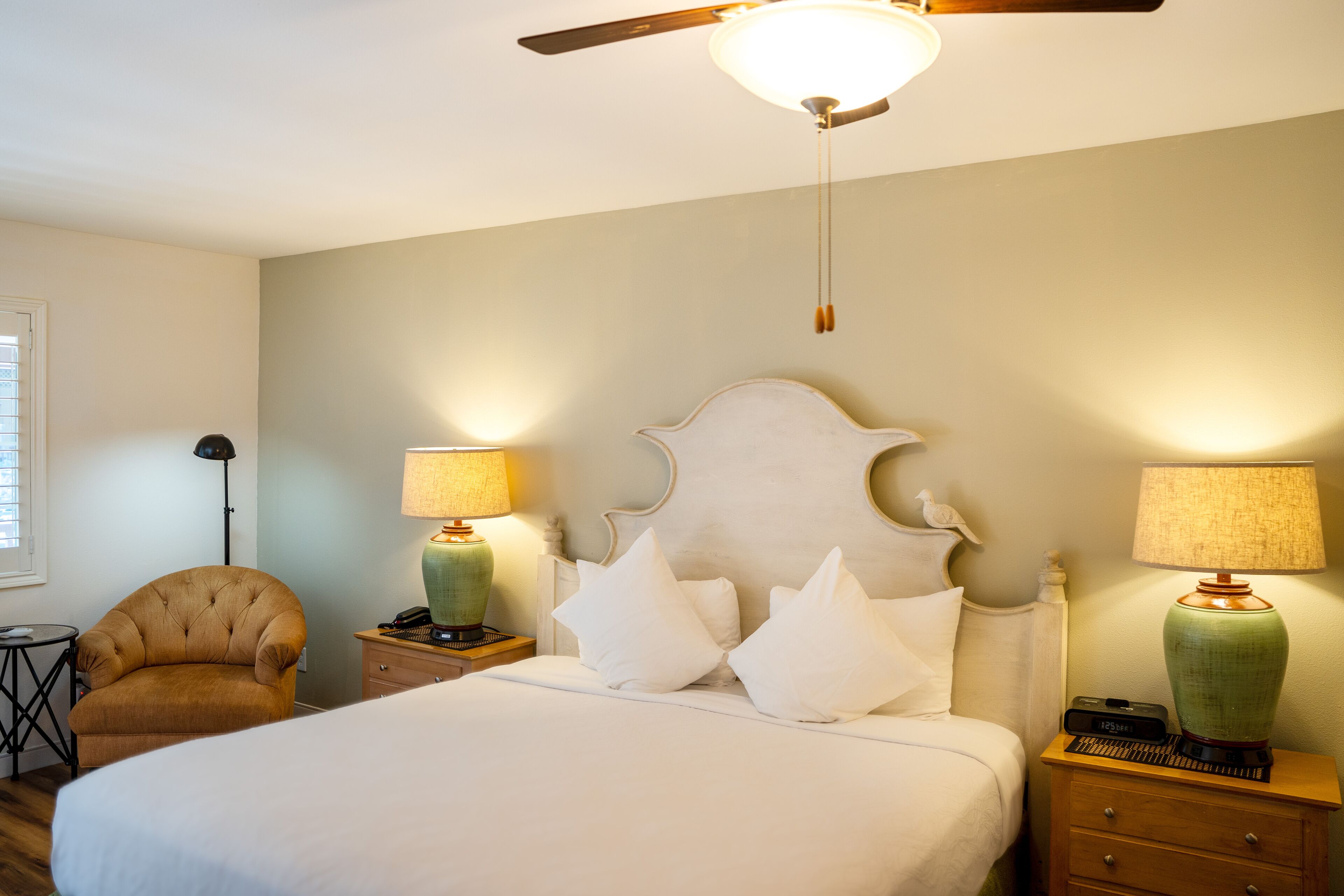 A bedroom with a bed, two nightstands, a chair, a ceiling fan, and two lamps.