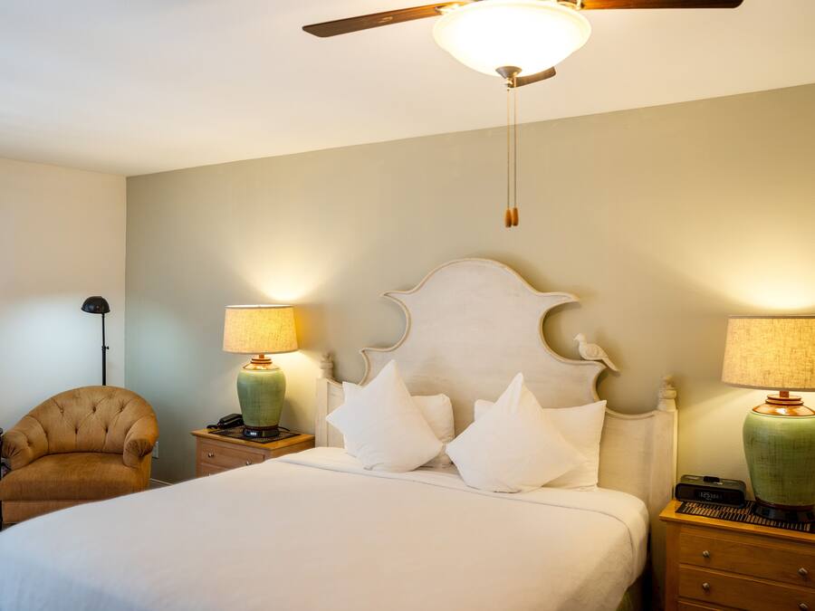 A bedroom with a bed, two nightstands, a chair, a ceiling fan, and two lamps.