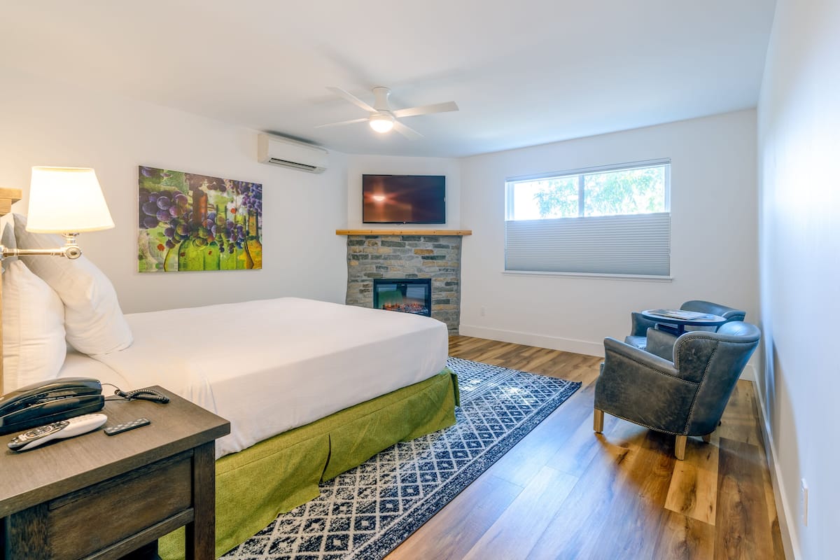 A bedroom with a bed, a nightstand, a chair, a fireplace, and a window.