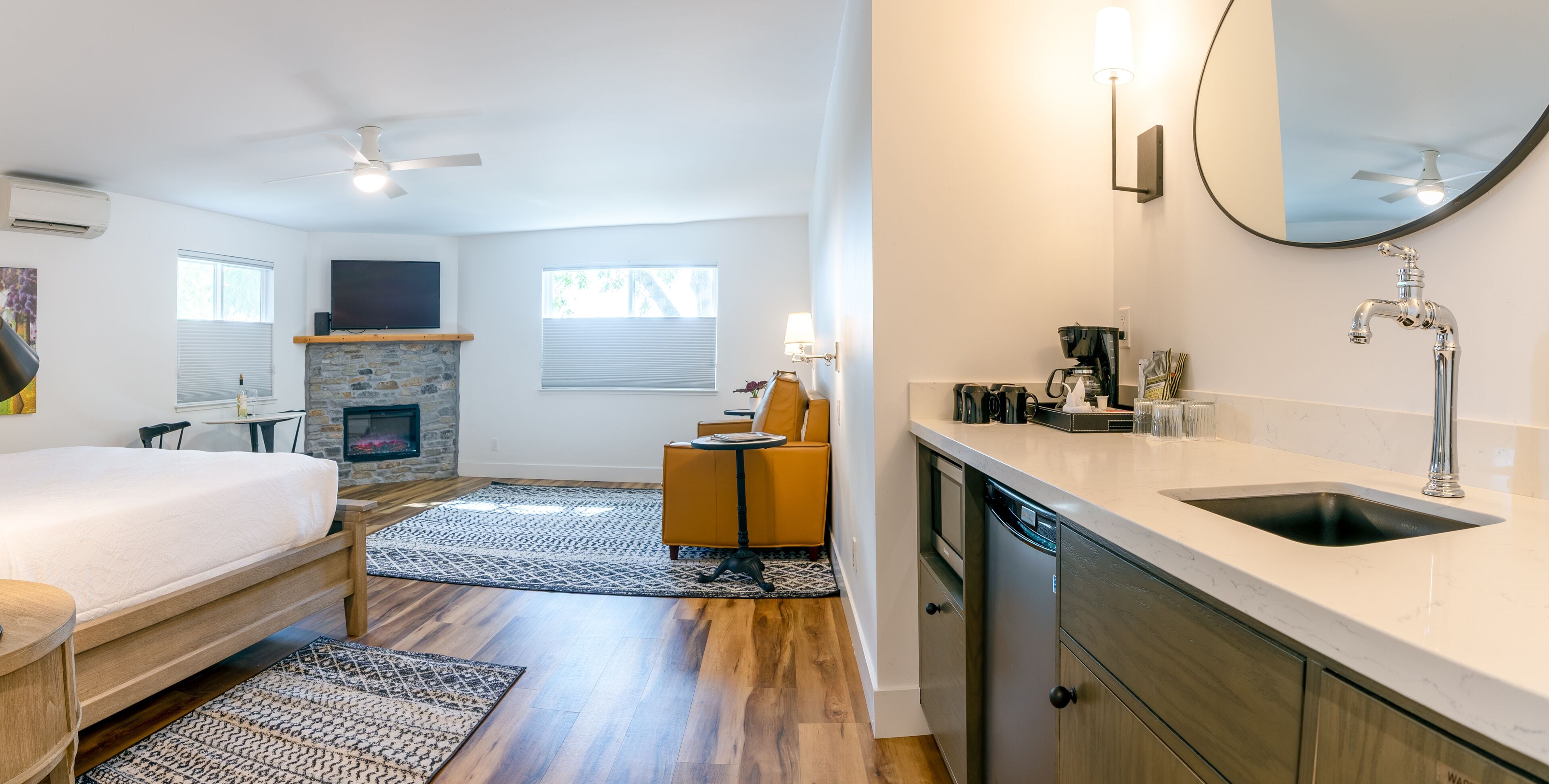 A modern bedroom with a bed, a fireplace, a dining area, and a kitchen with a sink and dishwasher.