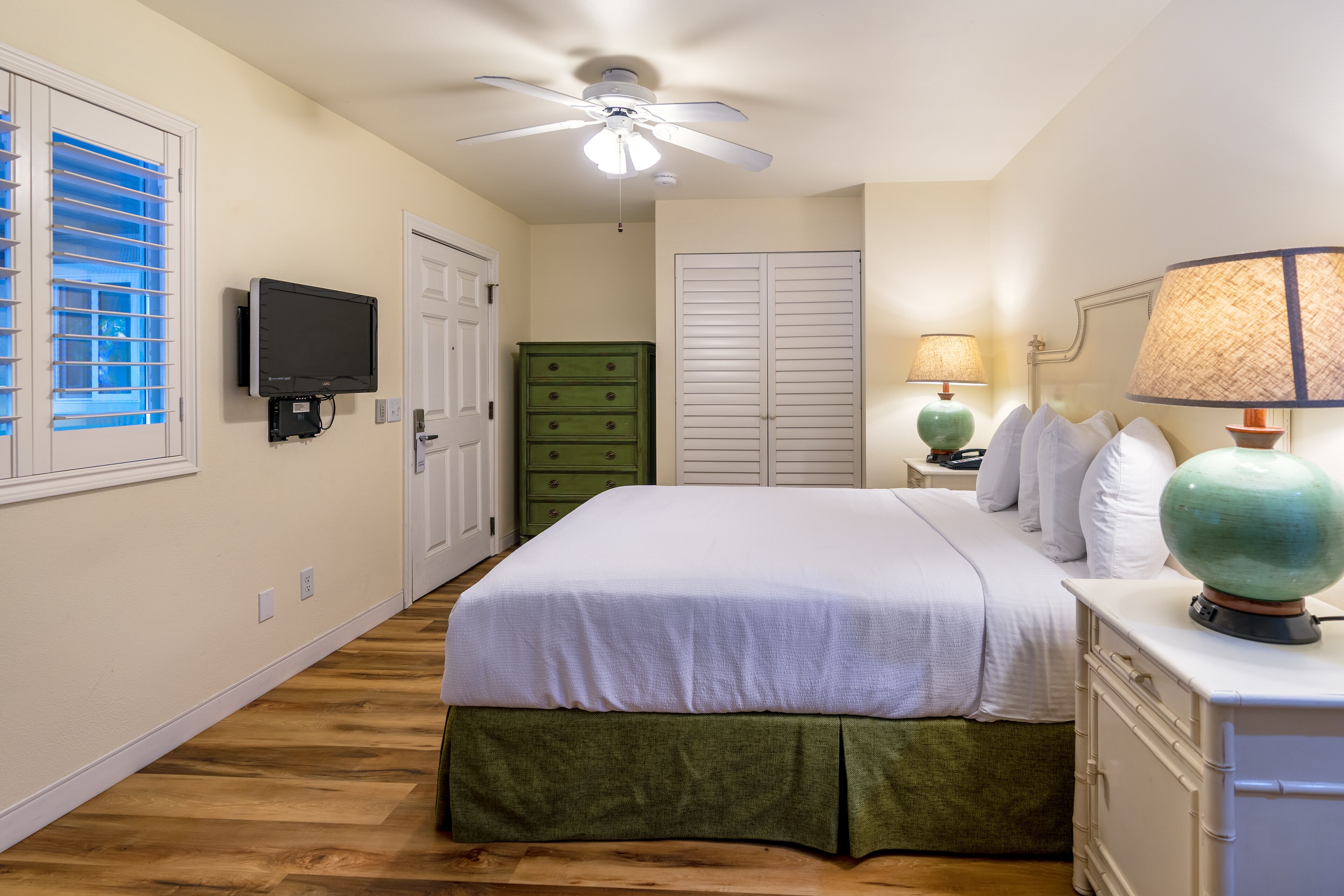 A bedroom with a bed, a ceiling fan, a television, a dresser, and a nightstand with lamps.