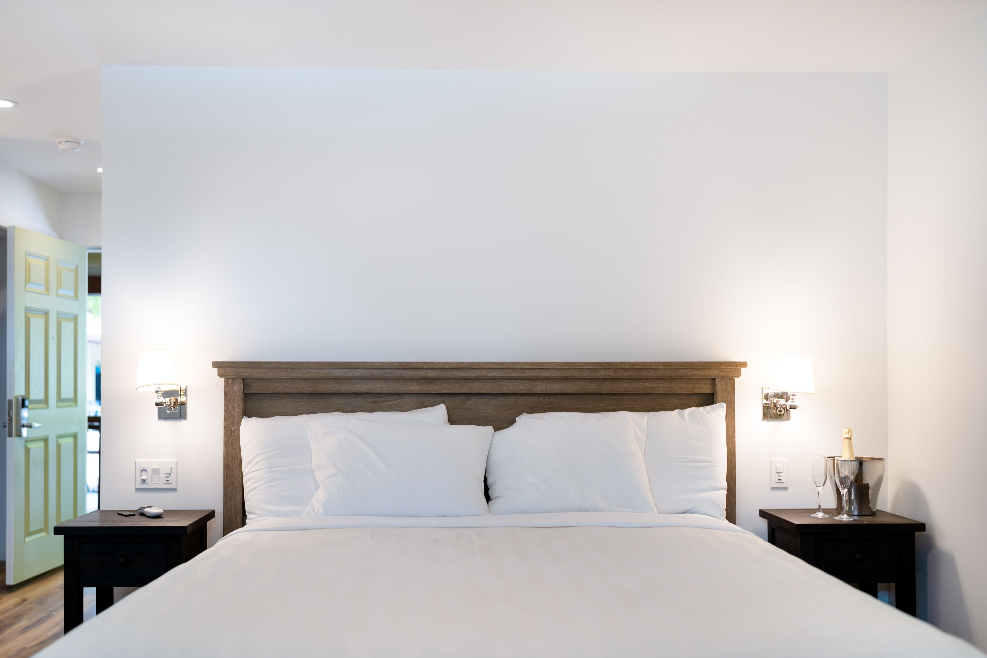 Een opgemaakt bed met witte lakens, twee nachtkastjes met lampen, en een houten hoofdbord.