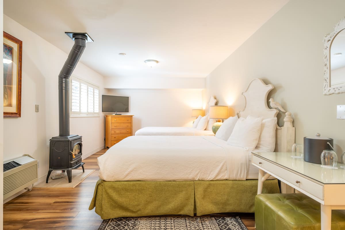 A bedroom with two beds, a wooden dresser, a TV, and a black stove.