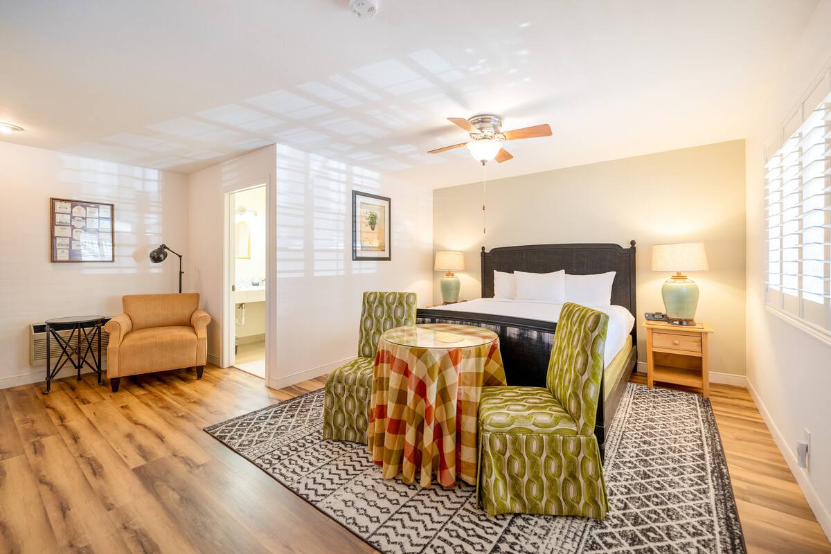 A hotel room with a bed, a chair, a table, and a ceiling fan.