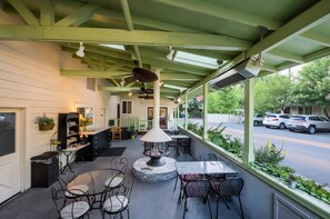 A covered outdoor seating area with tables and chairs, a fire pit, and a view of the street.