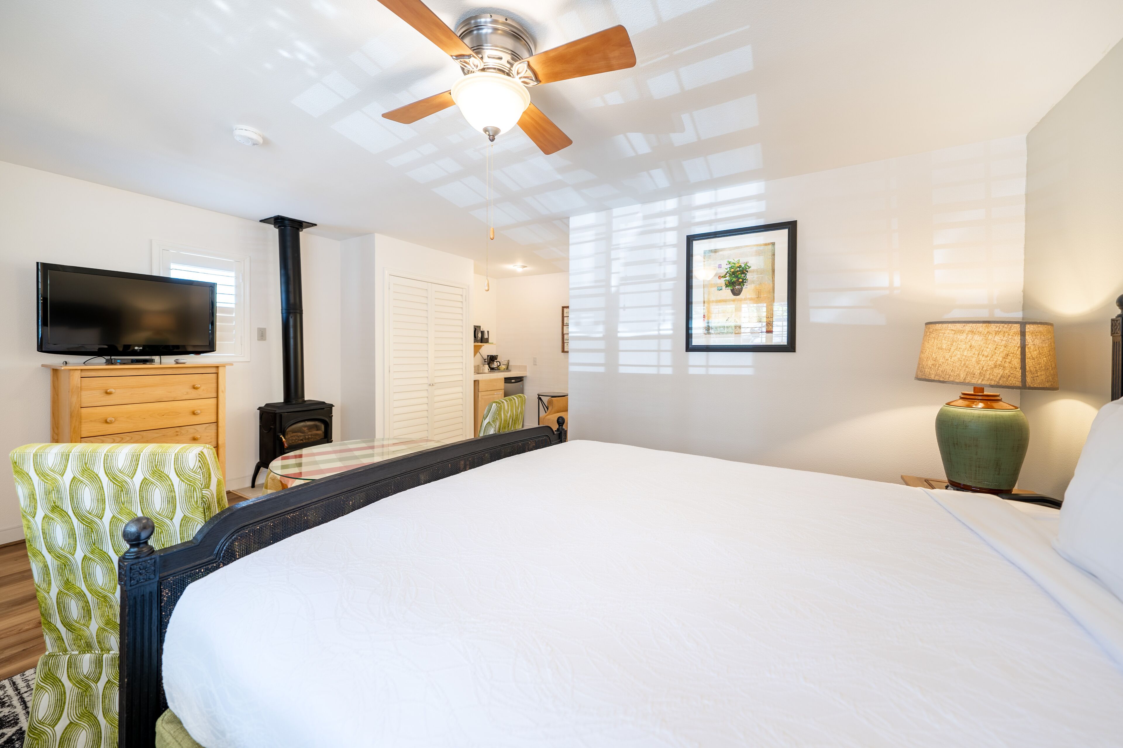 A spacious bedroom with a large bed, a ceiling fan, a television, and a fireplace.