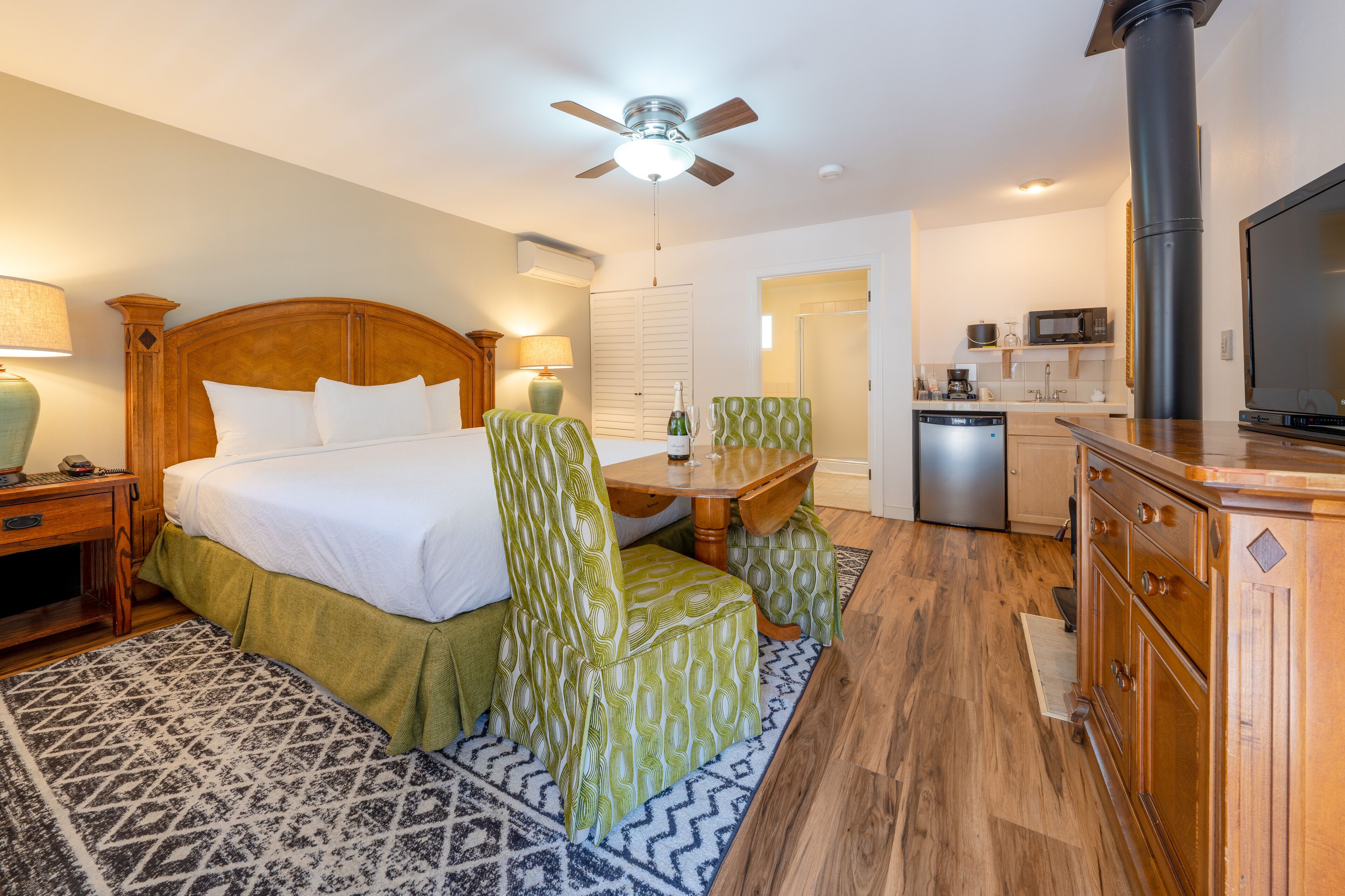 A hotel room with a bed, a desk, a chair, a television, a microwave, and a sink.