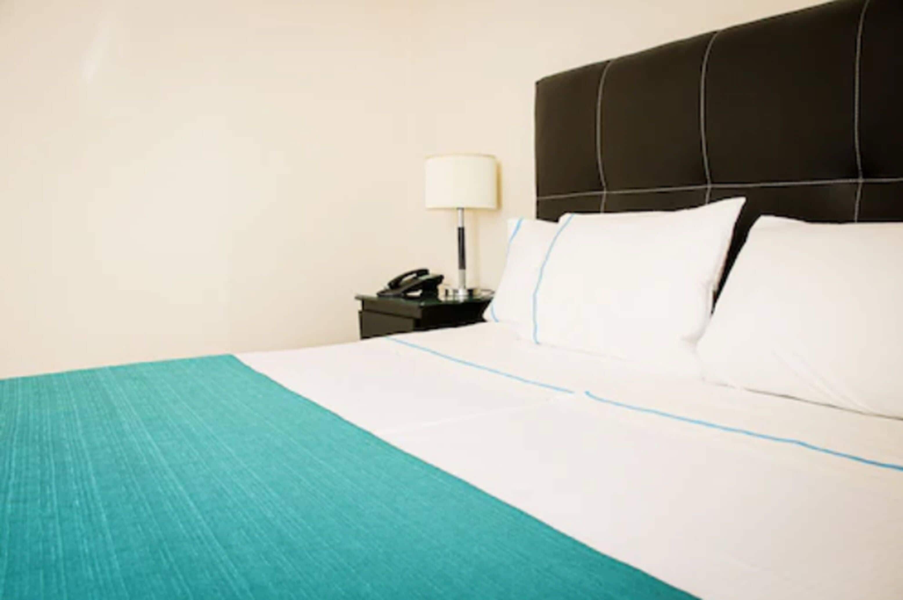 Una habitación de hotel con una cama, una mesita de noche con lámpara y un teléfono.