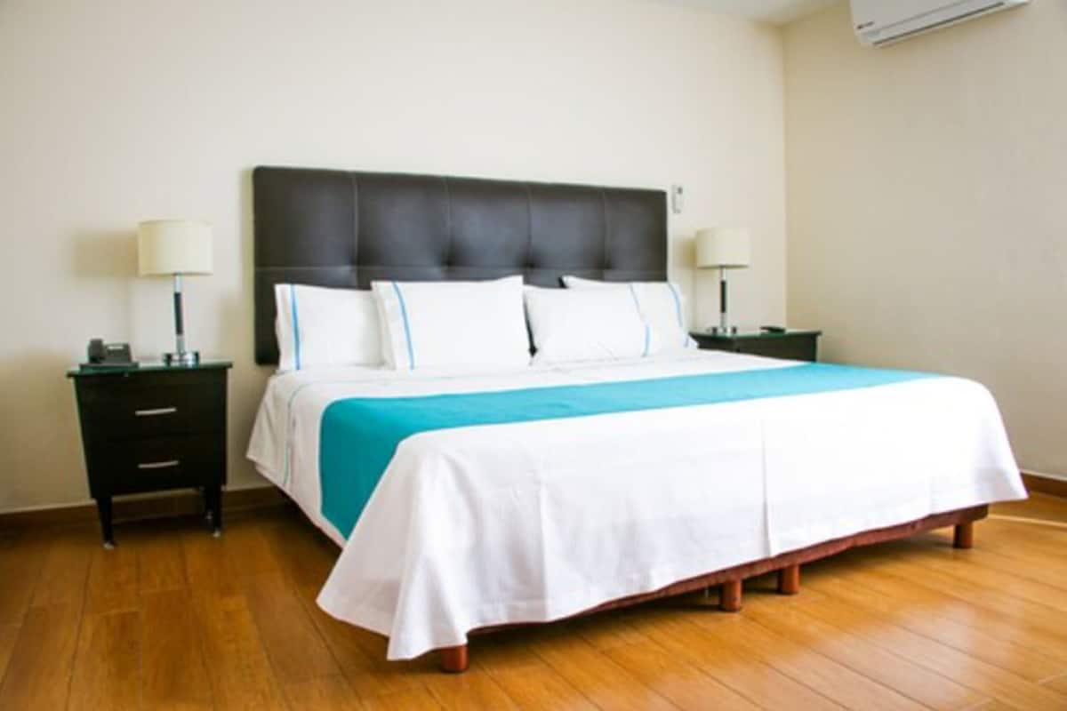 A hotel room with a large bed, two bedside tables, and an air conditioning unit on the wall.