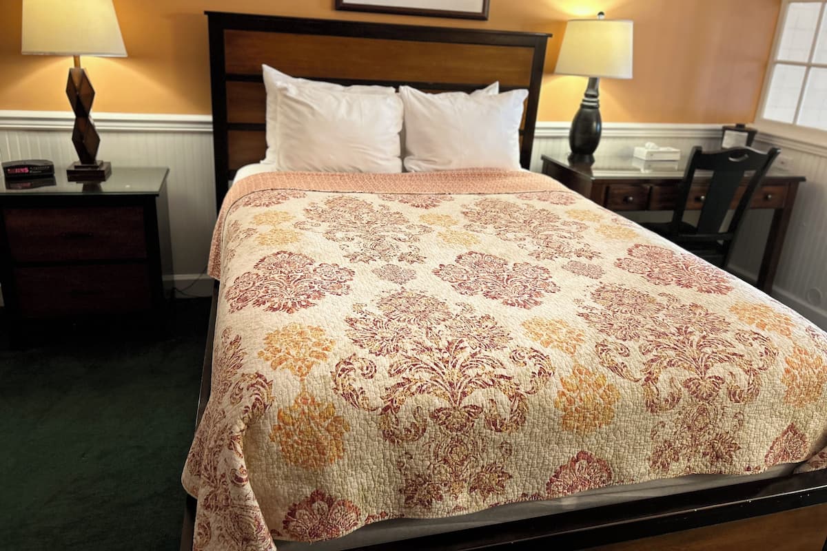 A neatly made bed with a patterned bedspread, two bedside lamps, and a framed picture on the wall.