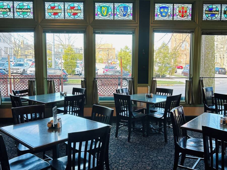 A restaurant with large windows, wooden tables, and black chairs.