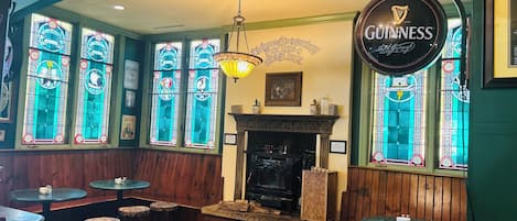 A cozy pub interior with a Guinness sign, stained glass windows, and a fireplace.