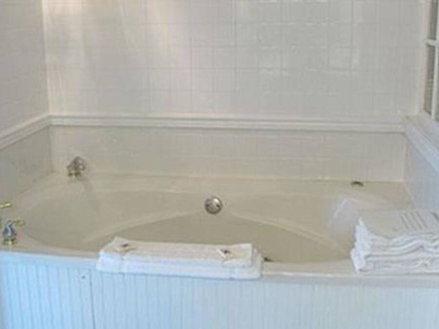 Eine weiße Badewanne mit einem Wasserhahn, ein kleines Fenster zur Rechten und ein Stapel weißer Handtücher an der Seite.