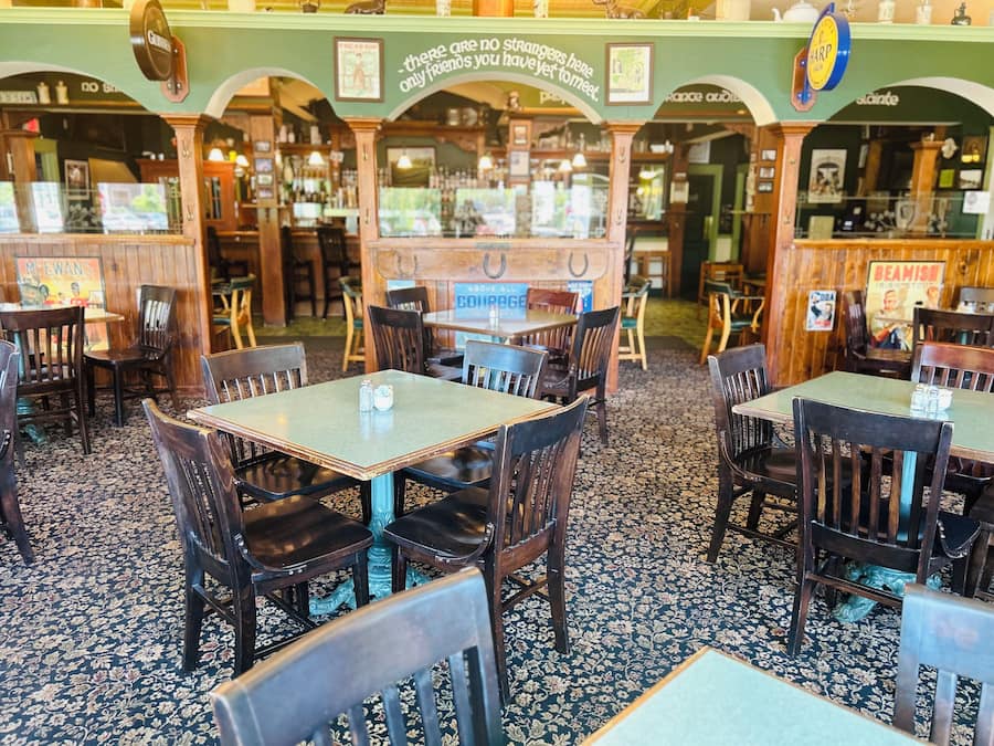 A restaurant interior with wooden tables and chairs, a bar area, and a patterned carpet.