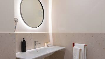 Un bagno con lavandino bianco, uno specchio, un portasciuga e un asciugacapelli.