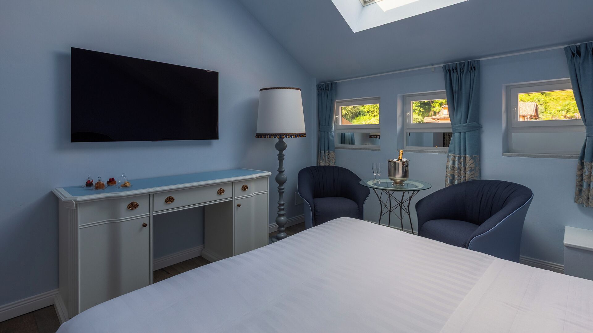 Une chambre à coucher avec un lit, un bureau, deux chaises, une télévision et une fenêtre avec des rideaux.