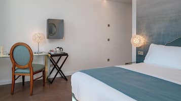 Una habitación de hotel con una cama, un escritorio con silla, una mesita y un espejo instalado en la pared.