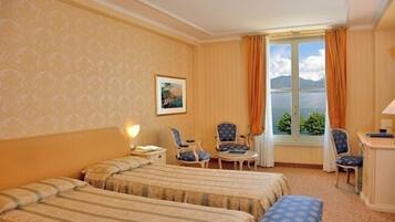 Camera d'albergo con due letti, una scrivania, due sedie, una lampada e una finestra che dà su cielo e montagne.