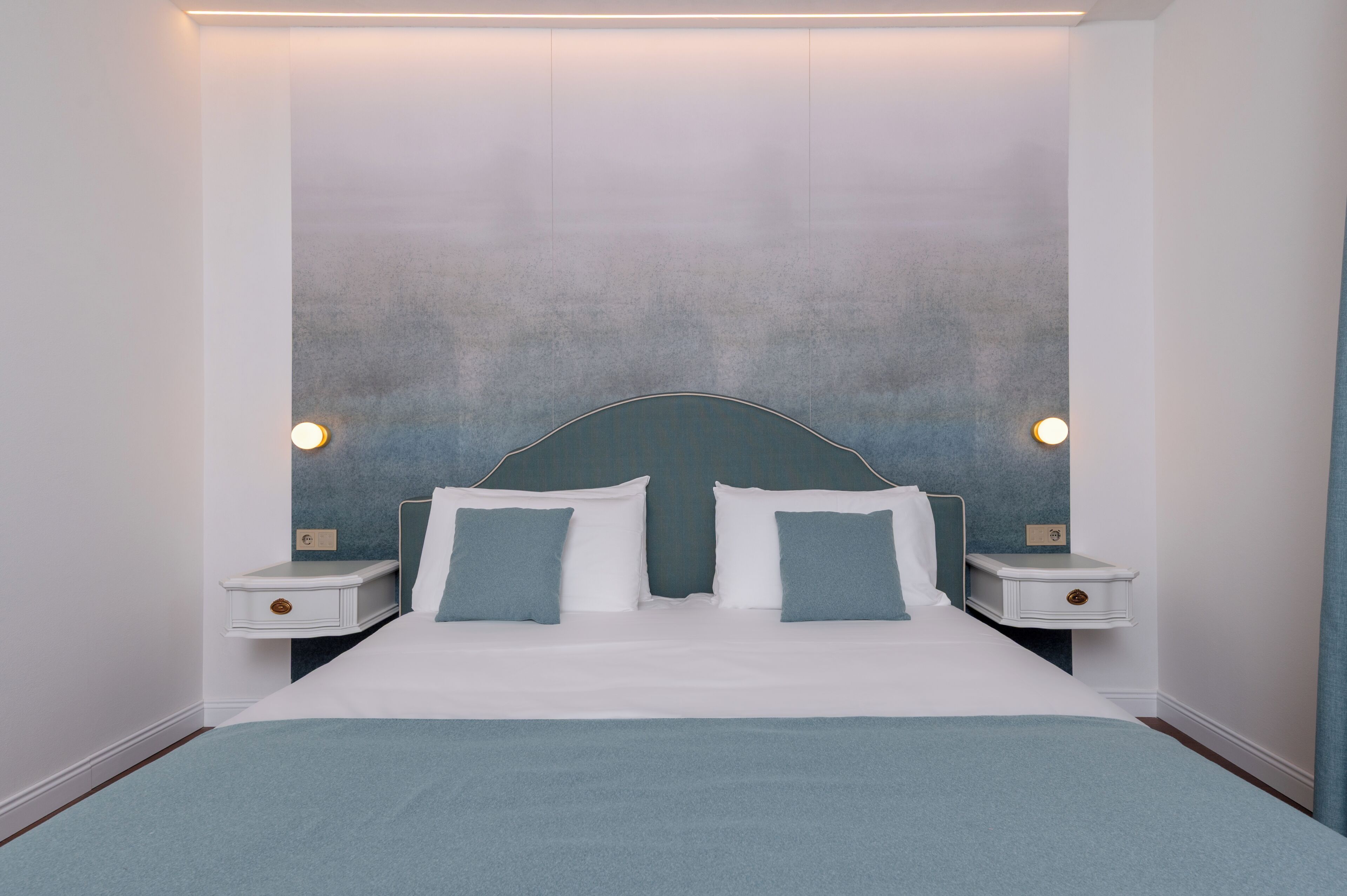 A neatly made bed with white and blue bedding, two bedside tables with lamps, and a textured wall behind the bed.