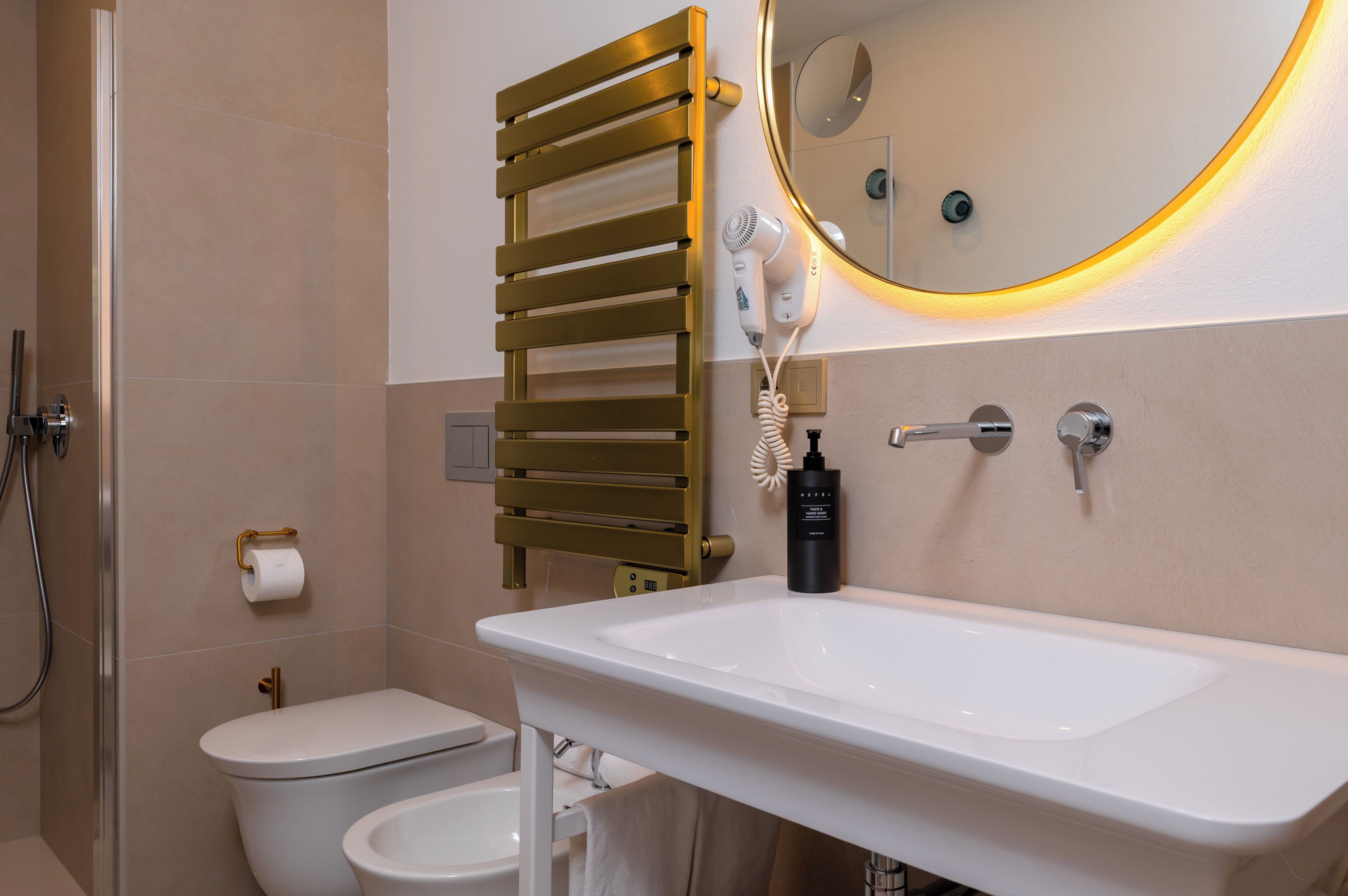 A bathroom with a white sink, a toilet, a towel rack, a hairdryer, and a mirror with a light.